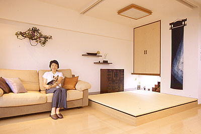 フローリングのLDKの一角に床より一段高い畳スペース。畳とフローリングの床、ソファー、収納の扉など統一された色調になっている。